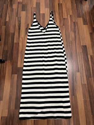 Svartvit långrandig klänning - Snygg långklänning med breda svarta och vita horisontella ränder. Klänningen har v-ringad hals och smala axelband, vilket ger en chill och modern vibe. Materialet är stickat och känns mjukt mot huden. Perfekt för dig som gillar enkel men stilren design.