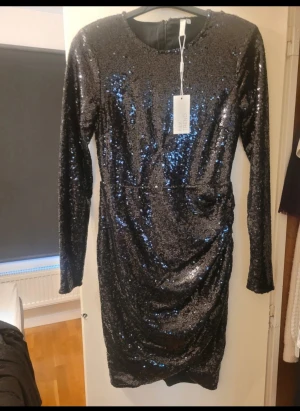 Svart paljettklänning från NLY Trend - Glittrig svart klänning från NLY Trend i storlek 36. Klänningen har lång ärm, rund hals och är täckt av svarta paljetter som ger en snygg och festlig look. Modellen är figurnära.