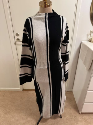 Randig lång stickad klänning Shein - Säljer en långärmad stickad klänning från Shein i storlek M. Klänningen är svart och vit med breda vertikala och horisontella ränder, har markerad midja och rak passform. Perfekt för dig som gillar en stilren och bekväm look.