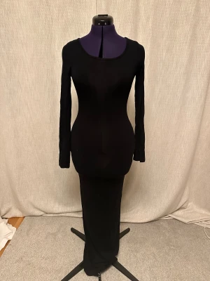 Svart långärmad långklänning skims doupe  - En stilren svart långklänning med lång ärm och rund halsringning. Klänningen är figurnära och har en minimalistisk design utan mönster eller detaljer. Materialet är stretchigt och mjukt, vilket ger en snygg och smickrande passform.