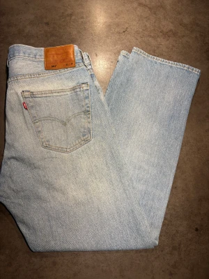 Archive Jeans Levis - Säljer ett par riktigt snygga ljusblåa Levis Jeans 501. De har en rak passform och lägger sig snyggt över skorna. Storlek:  W33 L30. Skriv vid frågor eller kom med bud!