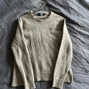 Grå Merinotröja från Polo Ralph Lauren - Säljer en stilren grå tröja från Polo Ralph Lauren i 100% extra fin merinoull. Tröjan har en klassisk rund hals och långa ärmar med ribbade muddar.