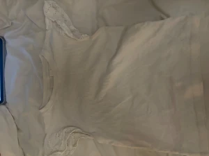 Vit ribbad topp med spetsärmar Gina Tricot - Supersöt vit topp från Gina Tricot i ribbad bomull med korta ärmar dekorerade med broderad spets. Perfekt för dig som gillar romantiska detaljer och vill ha en enkel men ändå unik look. Rund halsringning och figurnära passform.