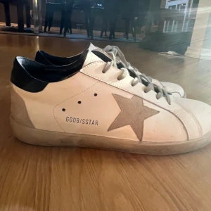 Golden Goose Superstar sneakers vit/grå - Golden Goose Superstar sneakers i vitt skinn med grå mockadetaljer och svart häl. Klassisk stjärna på sidan och GGDB/SSTAR-tryck. Skorna har storlek 43 och knappt använda! Hör jättegärna va dig vid funderingar till skon så svarar jag snabbt!💯pris ej hugget i sten!!!!