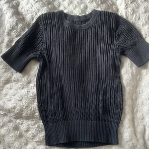 Ribbstickad svart kortärmad tröja - Säljer en svart ribbstickad tröja med korta ärmar och rund hals. Tröjan har en chunky, stickad struktur och breda muddar vid ärmslut och nederkant. Perfekt för lager-på-lager och funkar året runt. Den är från mango men lappen är av.