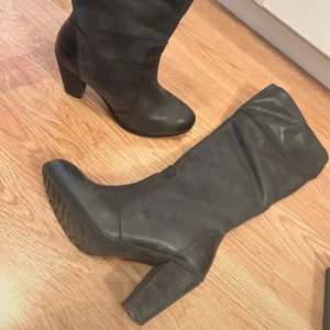 Svarta höga stövlar med klack - Snygga svarta stövlar med hög klack och rund tå. Stövlarna har dragkedja på insidan för enkel påtagning och en stilren design som passar till många outfits. Perfekta för dig som vill ha en klassisk look med lite edge