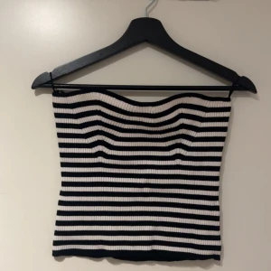 Tubtopp - Säljer en svartvit randig tubtopp från Gina Tricot i ribbat material. Toppen är axelbandslös och har en tight passform som sitter snyggt på kroppen. Perfekt att styla med jeans eller kjol för en trendig look. Aldrig använd💞