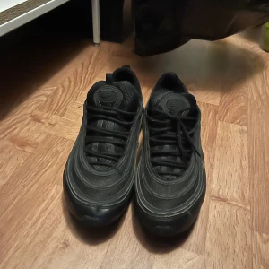 Svarta Nike Air Max 97 sneakers - Säljer ett par svarta Nike Air Max 97 sneakers med ikoniska vågformade detaljer och synlig luftbubbla i sulan. Använda några månader men kan hålla sig ett bra tag till därför erbjuder jag ett bra pris. Skriv om ni är intresserade😁!