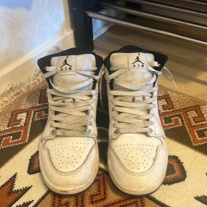 Nike Air Jordan 1 Mid vit/svart US9 - Säljer ett par Nike Air Jordan 1 Mid i vitt och svart. Klassisk high-top siluett med svart swoosh, perforerad tå och snörning. Skorna har svart foder och Air Jordan-logga på sidan. Perfekta för dig som gillar streetwear och sneakers med ikonisk design.