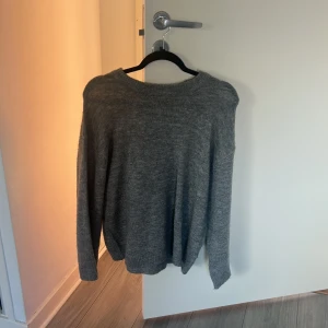 Grå stickad tröja med rund hals - En enkel och skön grå stickad tröja med rund hals och långa ärmar. Perfekt för kyliga dagar och passar till både jeans och mjukisbyxor. Tröjan har en loose passform och ribbade muddar vid ärmslut och nederkant.