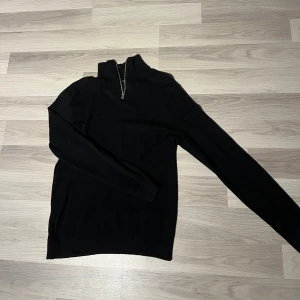 Quarter zip från Jack n Jones - Svart långärmad tröja från Jack & Jones med half zip-dragkedja i halsen. Tröjan har en stilren design med ribbade muddar och är gjord i mjuk bomull. Perfekt för dig som gillar enkel och clean stil.