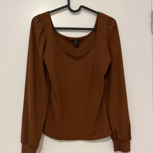 Brun långärmad topp med fyrkantig ringning - Säljer en brun långärmad topp  med snygg fyrkantig ringning och lätt puffade axlar. Toppen är ribbad och har en figurnära passform som passar perfekt till jeans eller kjol.