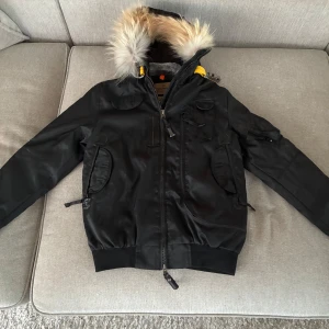 Svart Parajumpers jacka med pälsluva - Grym svart Parajumpers jacka med fluffig päls på luvan och coola gula detaljer. Jackan har flera fickor, dragkedja framtill och quiltat foder. Perfekt för kalla dagar och har en riktigt snygg streetstil. Kom med frågor om ni har några! Pris kan diskuteras 