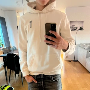 Vit hoodie med tryck  - Säljer en vit hoodie från h&m med stor grafisk print av en klassisk staty på ryggen och en liten pelare framtill. Tröjan har huva med snörning och känguruficka. 