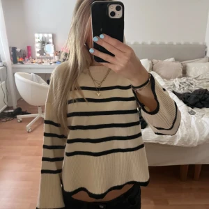 Randig stickad tröja från Bershka - Superfin stickad tröja från Bershka i beige med svarta ränder. Tröjan har en croppad passform, rund halsringning och långa ärmar. Perfekt till jeans för en chill och trendig look.