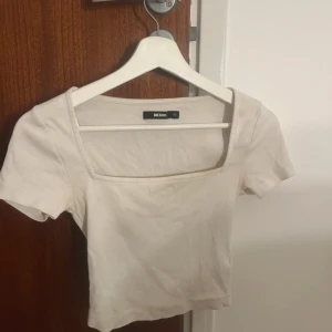 Vit ribbad topp från Bik Bok - Säljer en vit ribbad topp från Bik Bok med fyrkantig urringning och korta ärmar. Toppen är croppad och har en slim passform. 