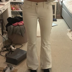 Vita bootcut jeans med hög midja - Säljer ett par vita jeans med bootcut-modell och hög midja. Byxorna har klassisk femficksdesign, bälteshällor och stängs med knapp och dragkedja. Materialet är stretchigt och mjukt, vilket gör dem riktigt sköna att bära.