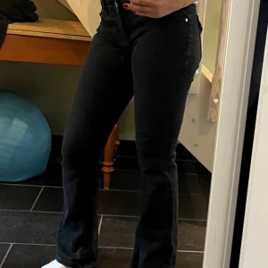 Svarta bootcut jeans med låg midja - Säljer ett par svarta jeans med bootcut-modell och låg midja. Jeansen har klassisk femficksdesign, silverfärgade nitar och dragkedja.  Perfekta till sneakers eller boots.