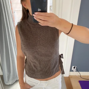 Brun ribbad polotopp med knyt i sidan - Säljer en brun ärmlös polotopp i ribbstickat material med hög krage och snygga knytband i sidorna som går att justera 