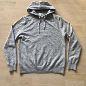 Grå hoodie i kashmir från ONEWear - Mjuk och stilren grå hoodie från ONEWear i kashmir. Tröjan har huva med snörning, ribbade muddar och lång ärm. Perfekt för dig som gillar en clean look och vill ha något riktigt skönt och lyxigt i garderoben.