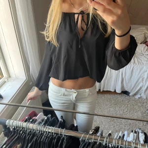 Svart croppad blus med snörning - Säljer en svart croppad blus med långa ärmar och elastiska muddar. Toppen har snörning framtill vid halsen och kan bäras offshoulder för en cool look. Tunt och flowy material som känns lätt och luftigt.