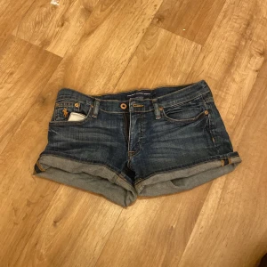 Jeansshorts från Ralph Lauren Sport - Snygga mörkblå jeansshorts från Ralph Lauren Sport med klassisk femficksdesign, uppvikta ben och ikonisk broderad logga på fickan. Tillverkade i stretchig denim av bomull och lite elastan för skön passform. Perfekta för sommardagar och enkel att matcha.
