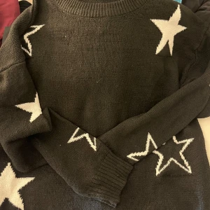 Svart stickad tröja med stjärnor - Svart stickad tröja från SHEIN i storlek XL med vita stjärnor på ärmar och axlar. Tröjan har rund halsringning och långa ärmar. Perfekt för dig som gillar en cool och avslappnad stil.