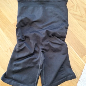 Svarta shaping-shorts från bpc, L - Svarta shaping-shorts från bpc med hög midja och sömlös design. Materialet är stretchigt polyester och elastan, vilket ger en tight och bekväm passform. Baksidan har snygga rynkdetaljer för extra form. Perfekta under klänning eller kjol för en smickrande siluett. Helt nya.