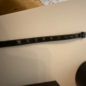 Svart Valentino bälte med nitar - Säljer ett svart armband från Valentino Garavani i äkta skinn med nitar i metall längs hela bandet. Har knappt använt armbandet och finns inga tecken alls på användning. Nypris ligger på cirka 3000kr på deras hemsida där jag köpt den ifrån. Kvitto och allt annat medkommer. Det är bara att höra av er om ni undrar något.