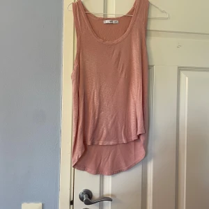 Rosa linnetopp från MNG Basics - Säljer en ljusrosa ärmlös linnetopp från MNG Basics. Toppen har rund halsringning och längre bakstycke för en snygg layering-effekt. Tillverkad i mjuk bomullsmix, perfekt för varma dagar eller som basplagg.