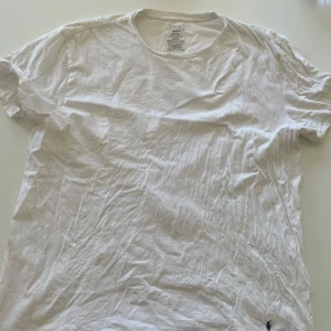 Vit t-shirt från Polo Ralph Lauren XL - Klassisk vit t-shirt från Polo Ralph Lauren i storlek XL. Tillverkad i 100% bomull med rund hals och korta ärmar. Diskret broderad logga i mörkblått nertill. Perfekt basic-plagg med clean look och skön passform.