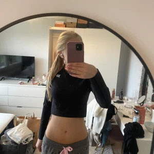 Svart croppad långärmad träningstopp 157 - Svart croppad långärmad träningstopp från 157 med rund halsringning och diskret logga på bröstet. Toppen är tight och har en stilren design i mjukt, stretchigt material som passar perfekt till gymmet eller löprundan.