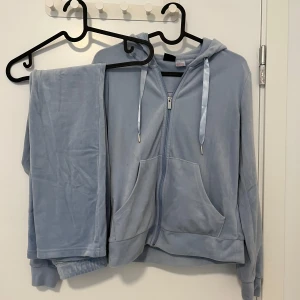 Ljusblå velour hoodie med dragkedja - Supermjuk ljusblå hoodie i velour med dragkedja framtill, huva och snörning. Tröjan har kängurufickor och långa ärmar. Perfekt för chill dagar eller när du vill vara extra comfy.