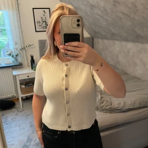 Vit ribbad kortärmad topp Gina Tricot - Säljer en vit ribbad topp från Gina Tricot med korta ärmar och rund hals. Toppen har knappar framtill och är stickad i ett mjukt material. Perfekt att styla med jeans eller kjol för en clean look.