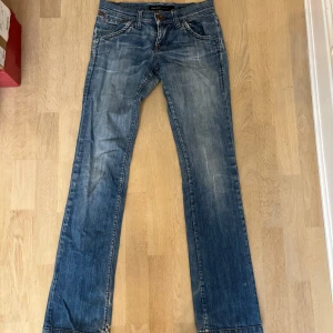 Miss Sixty blå bootcut jeans Blitz - Snygga blå jeans från Miss Sixty, modell Blitz, med klassisk bootcut och slitna detaljer på bakfickorna. Jeansen har normal passform, fem fickor och coola slitningar för en avslappnad look. Perfekta för dig som gillar retrovibbar och streetstyle. Storlek 26!🩷
