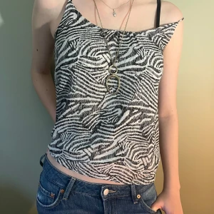 Zebramönstrad linnetopp med tunna band - Säljer en snygg zebramönstrad linnetopp i svart och vitt med tunna axelband. Toppen har en avslappnad passform och är perfekt för dig som gillar djurmönster och vill sticka ut. Materialet känns lätt och luftigt, perfekt för varmare dagar.