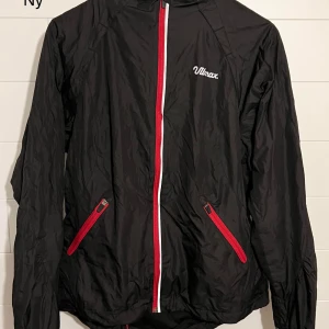 Svart vindjacka från Ulmax med röda detaljer - Svart vindjacka från Ulmax med röda dragkedjor och vita detaljer. Jackan har två fickor framtill och en hel dragkedja. Perfekt för blåsiga dagar och har en sportig look som sticker ut.