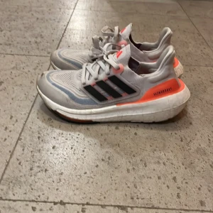 Adidas Ultraboost sneakers vit/orange - Säljer ett par Adidas Ultraboost sneakers i vitt med svarta ränder och orange detaljer. Skorna har en chunky sula och är tillverkade i mesh och syntetmaterial. Perfekta för dig som gillar sportig stil och vill ha bekväma skor med snygg design.