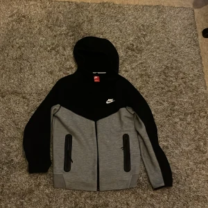 Nike hoodie svart och grå S - Nike hoodie i svart och grått med dragkedja framtill och två fickor med svarta dragkedjor. Klassisk logga på bröstet och huva. Perfekt för chill eller träning, snygg och sportig look.