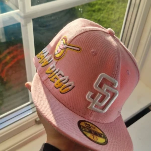 San Diego Padres rosa keps New Era - Snygg rosa keps från New Era med San Diego Padres brodyr i vitt och gult. Klassisk 59FIFTY-modell med platt skärm och broderade detaljer, inklusive SD-logga och basebollträ. Perfekt för dig som vill sticka ut med sportig stil.
