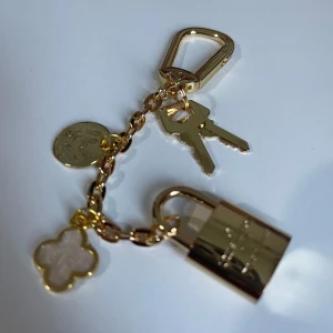 ✨ Lyx och elegans i ett: Nyckelring med guldfärgade charms ✨ - En stilren detalj som speglar din personlighet! Denna nyckelring med flera eleganta hängsmycken kombinerar funktionalitet med sofistikerad design.🔐 Höjdpunkter: 	•	Högkvalitativ metall med guldfärgad yta 	•	Dekorativa hängsmycken i form av lås och nyckel 	•	Fyrklöverdetalj i pärlvit nyans för en elegant touch•	Kan användas som både väskdekoration och nyckelring  💼 Perfekt för att lyfta din vardagsstil eller som en lyxig gåva till någon du tycker om! 