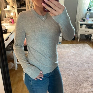 Grå stickad tröja med rund hals - Säljer en enkel och stilren grå stickad tröja med rund halsringning. Tröjan har långa ärmar och ribbade muddar vid ärmslut och nederkant. Perfekt att matcha med jeans för en clean och chill look.