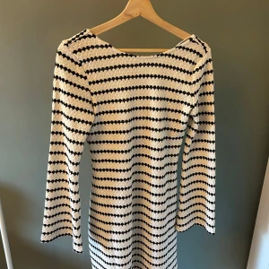 Randig stickad klänning med vida ärmar - Superfin stickad klänning med brunvita ränder och vida långa ärmar. Klänningen har en snygg rundad ringning fram och är figurnära upptill med lite utsvängd nederdel. Perfekt för dig som gillar retrovibbar och vill sticka ut med ett coolt mönster.