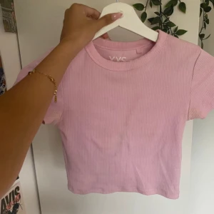 Ljusrosa ribbad croppad topp - Säljer en ljusrosa croppad topp från YVS. Toppen är ribbad med korta ärmar och rund halsringning. Perfekt till jeans eller kjol för en chill och snygg look. Materialet är mjukt och stretchigt, vilket gör den superbekväm att bära.