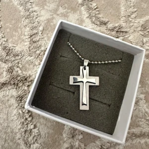 Silverfärgat korshalsband med kulkedja - Stilrent halsband med ett kors i silverfärg och snyggt urfräst mönster. Hängs i en klassisk kulkedja som ger en modern vibe. Perfekt accessoar för dig som gillar enkel men uttrycksfull design. Steinless steel 