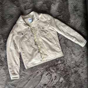 Beige mockajacka från Zara, stl S - Snygg beige mockajacka från Zara i storlek S. Jackan har klassisk jeansjacke-modell med två bröstfickor med knappar och två sidofickor. Mjuk yta och stilren look, perfekt för dig som vill ha en clean och trendig jacka.