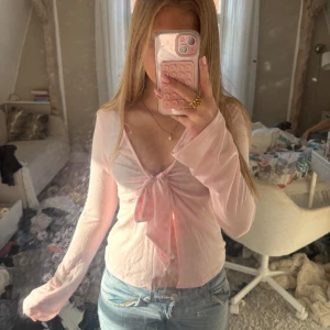 Ljusrosa långärmad topp Gina Tricot - Supersöt ljusrosa långärmad topp från Gina Tricot med djup v-ringning och knyt framtill. Tunn och lätt i materialet, perfekt för lager-på-lager eller som statement-piece. Sitter snyggt och har en feminin vibe.