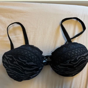 Svart zebramönstrad bj - Snygg svart bh med zebramönster och spetsdetaljer upptill. Axelbanden är justerbara och framtill finns en liten rosett. Storleken är 65a. Priset går att diskuteras!