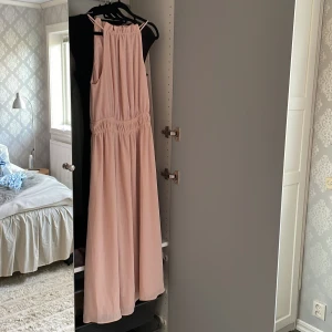 Ljusrosa långklänning med smala axelband - Superfin ljusrosa långklänning med smala axelband och rynkade detaljer i midjan. Klänningen har en flowy passform och är tillverkad i ett tunt, mjukt tyg som faller snyggt.  💗