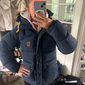 Fjällräven Expedition dunjacka marinblå - !!INTRESSEKOLL!! Byter gärna mot en svart i xxs/xs! Marinblå Fjällräven Expedition Series dunjacka med gul snörning i huvan, emblem på bröstet och stora fickor med knappar. Köpt vintern 2023 men sparsamt använd så ännu i perfekt skick! Pris kan diskuteras